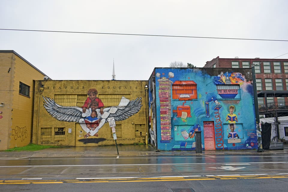 Pre-renovation street view of the building's concrete-block facade painted yellow, with a colorful mural on the adjacent wall.