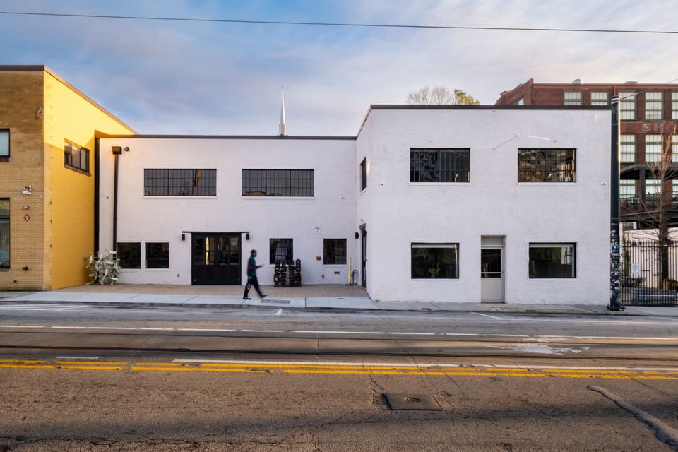The same building after renovation, seen from the same street angle, with a clean white-painted brick facade and black-framed windows and doors.