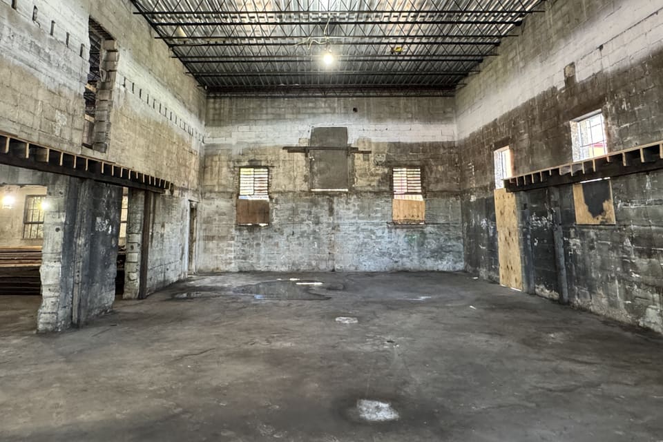 The future multi-purpose room mid-demolition, with concrete-block walls, a metal ceiling grid, and construction debris on the floor.