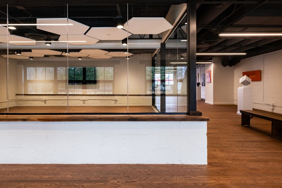 The same second-floor room finished as a conference room, with warm wood flooring, white walls, and an exposed black-steel ceiling structure.