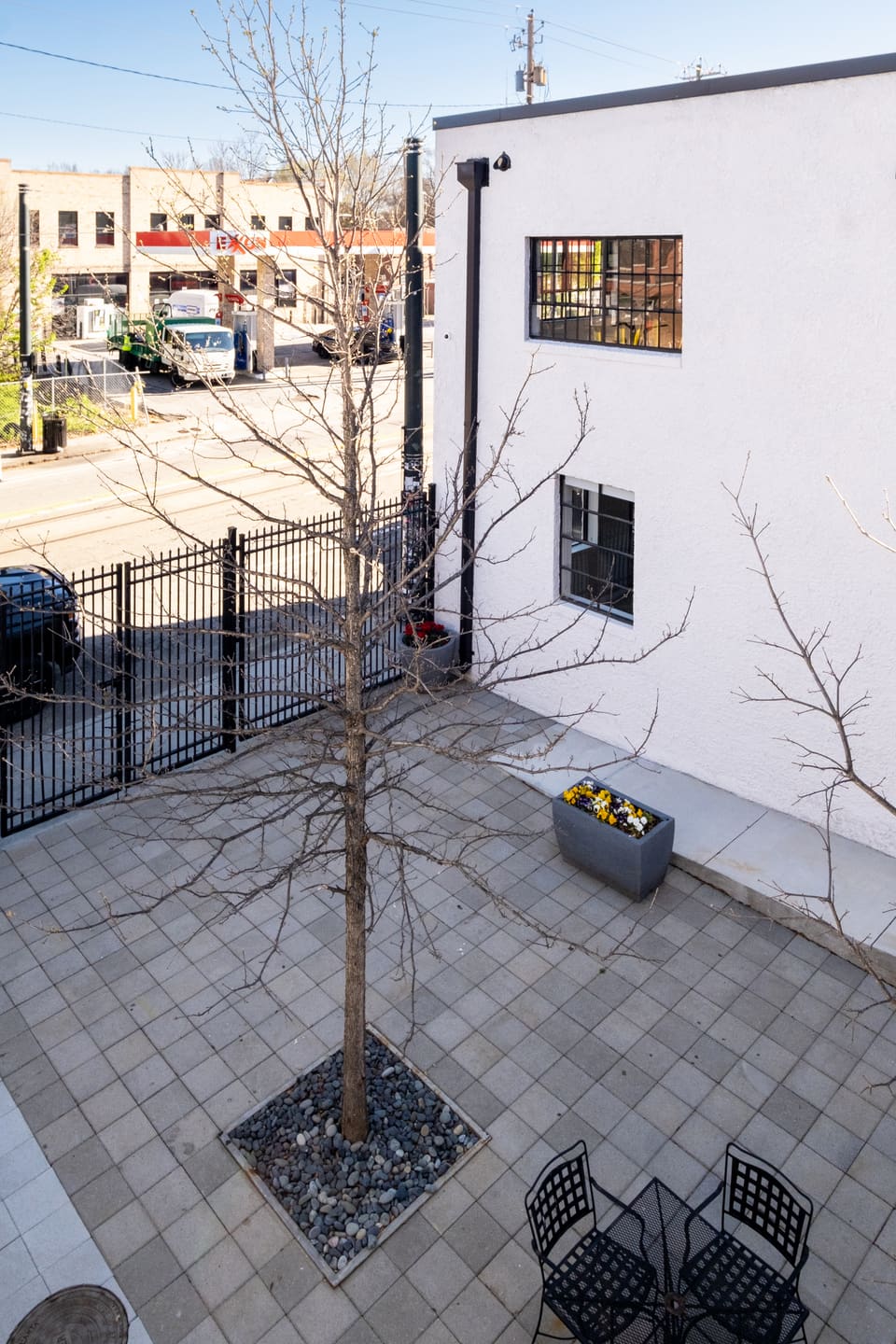 Split-level courtyard event space with black metal railings, concrete paving, and scattered seating between the two buildings.
